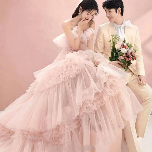 A woman in a voluminous pink tulle wedding gown and a man in a cream suit sit together.