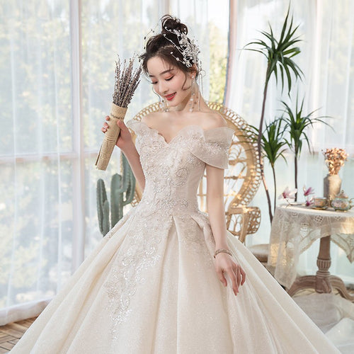 Woman in an off-the-shoulder sparkling ivory ball gown holding a dried bouquet indoors.