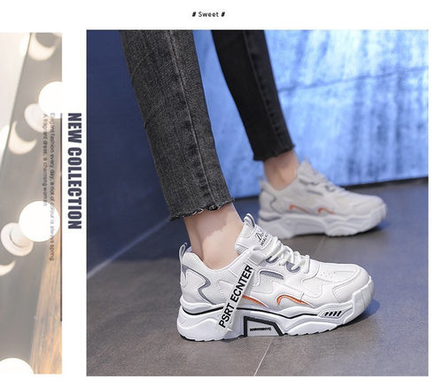 White chunky platform sneakers with grey and orange details and a branded strap worn on feet.