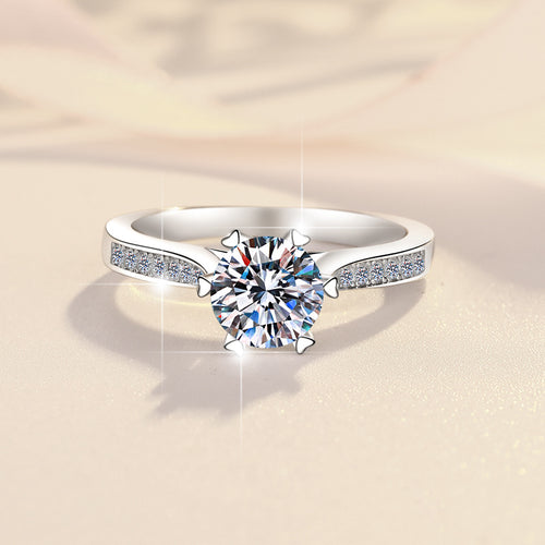 A silver ring with a large round center stone and pave-set diamonds along the band on a light background.