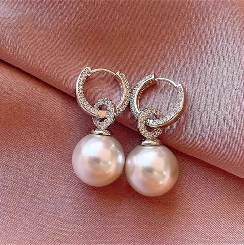 Silver hoop earrings with crystal-paved rings and large white pearl drops on pink silk.
