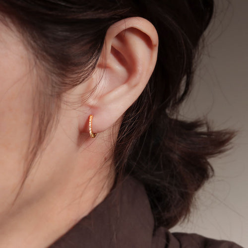 Small gold hoop earring encrusted with tiny gemstones, worn in an earlobe.