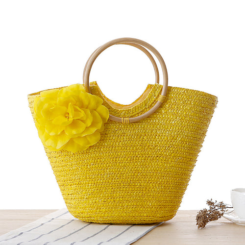 Yellow woven rattan beach bag with round wooden handles and a large yellow flower decoration.