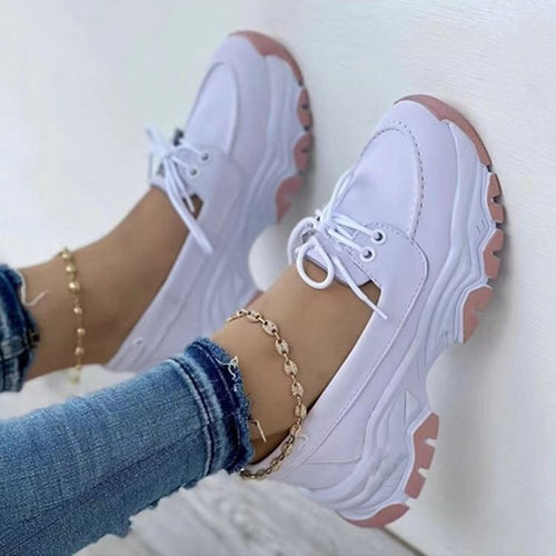 White chunky lace-up shoes with pink soles worn with blue jeans and gold anklets.