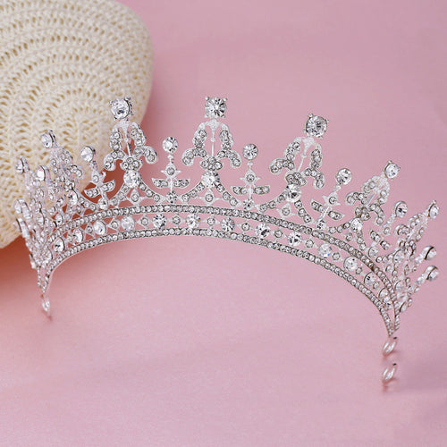 Silver rhinestone bridal tiara with intricate floral and scroll patterns against a pink background.
