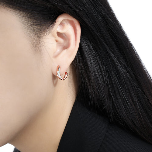 Close-up of a person wearing a small, irregular rose gold hoop earring encrusted with tiny diamonds.