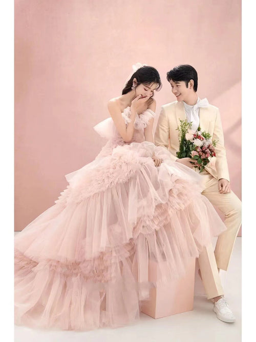 A bride in a voluminous pink tulle wedding dress sits with a groom in a cream suit holding flowers.