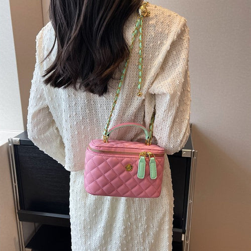 A person wearing a quilted pink leather vanity shoulder bag with mint green accents and a gold chain strap.