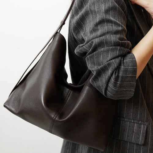 Dark brown leather slouchy shoulder bag worn by a person in a pinstripe blazer.