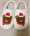 White fluffy slippers featuring a brown bear with a red Santa hat and scarf.
