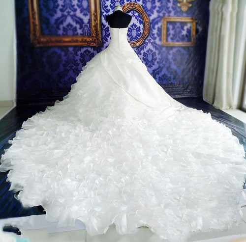 White strapless bridal gown on a mannequin with a massive ruffled, tiered train spreading across the floor.