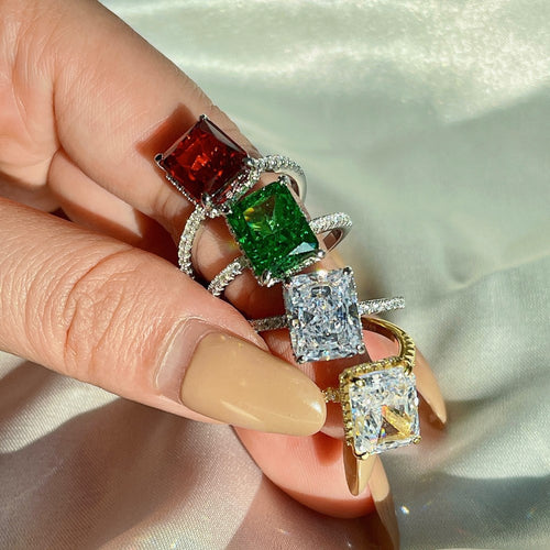 Four sterling silver rings with rectangular gemstones in red, green, clear, and gold worn on fingers.