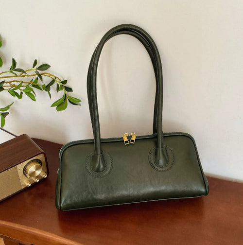 Dark green leather shoulder bag with two long straps and gold zippers on a wooden surface.