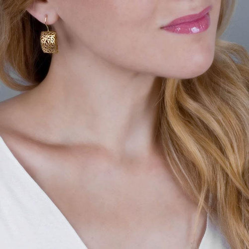 Close-up of a woman wearing a gold-colored, hollow alloy filigree hoop earring.