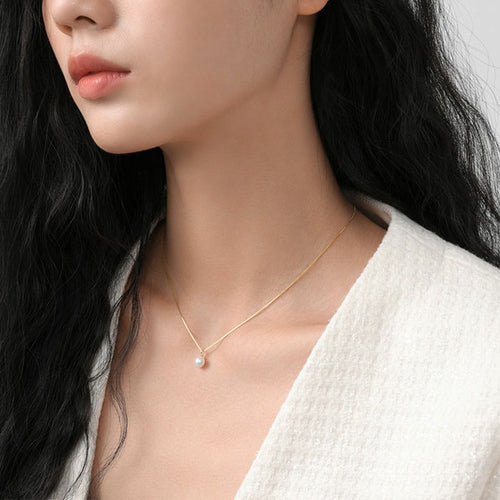 A person wearing a delicate gold chain necklace with a single round white pearl pendant.