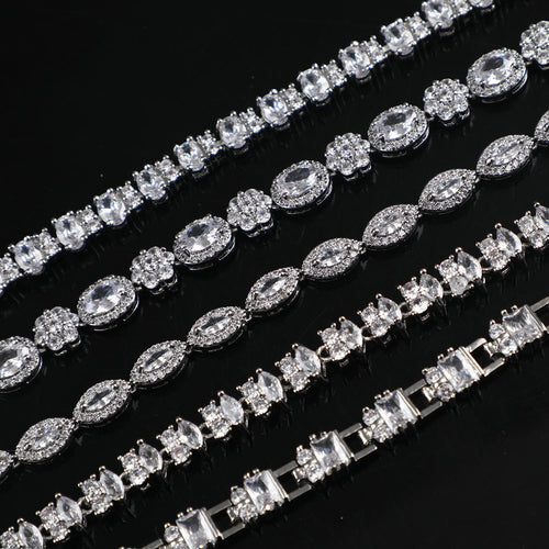 Five silver tone crystal armbands in varying gemstone shapes and patterns on black.