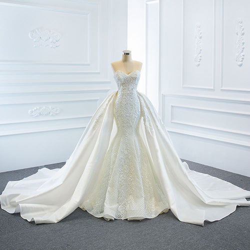 White strapless mermaid wedding dress with lace embroidery and a long overskirt on a mannequin.