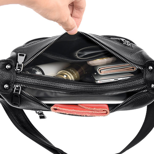 Open black leather shoulder bag with multiple compartments, filled with personal items.
