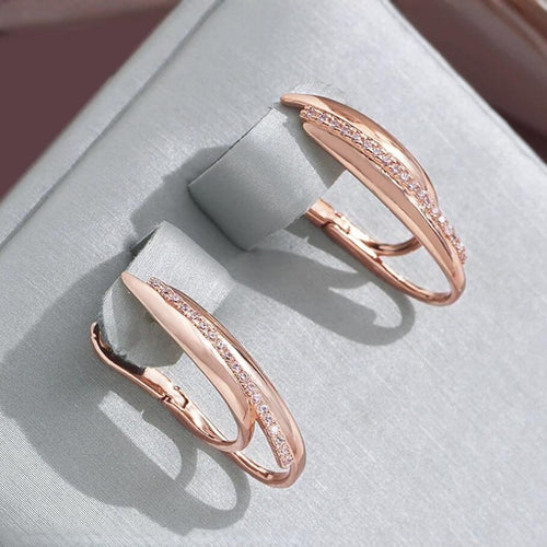 Rose gold hoop earrings with small cubic zirconia stones on display on a light gray stand.