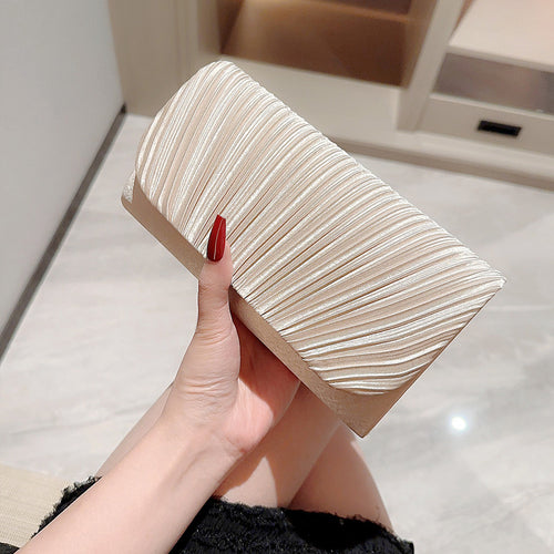 Hand holding a rectangular beige pleated clutch purse made of shiny fabric.