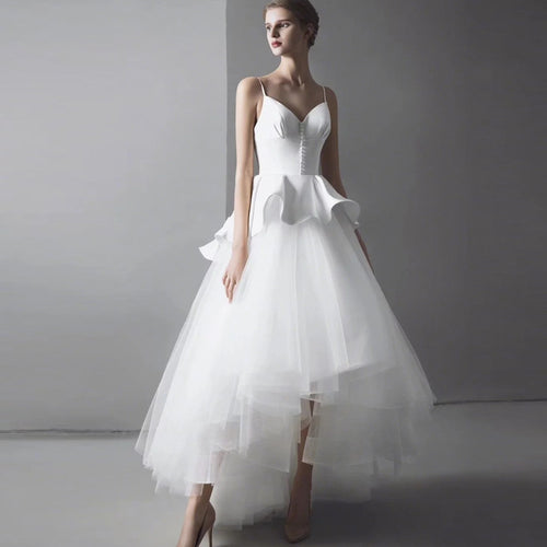 A white bridal gown with spaghetti straps, peplum waist, and layered tulle high-low skirt.
