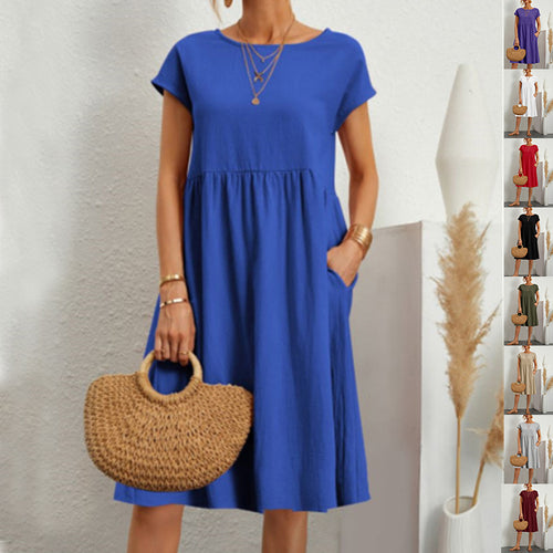 A woman wearing a royal blue round-neck knee-length dress with short sleeves and pockets, holding a woven bag.