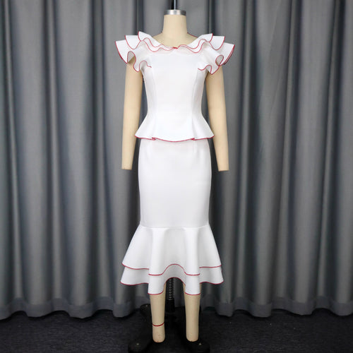 White two-piece fishtail skirt suit with red-trimmed ruffles on shoulders and hem, on mannequin.