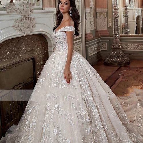 A model in an off-shoulder, lace ballgown wedding dress with floral embroidery and a full skirt.